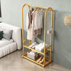 Gold clothing rack with clothes in a room with a sofa and lamp.