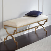 Decorative bench with gold legs and white cushion on a dark wooden floor.