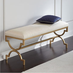 Decorative bench with gold legs and white cushion on a dark wooden floor.