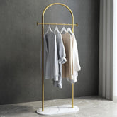 Gold clothing rack with white garments against a gray wall