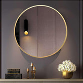 Round gold-framed mirror on a dark wall with decorative items below.