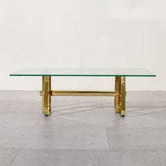 Glass coffee table with gold metal legs on a light wooden floor.