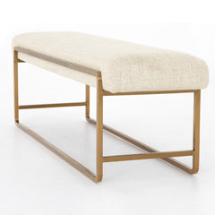 Beige upholstered bench with gold metal frame on a white background