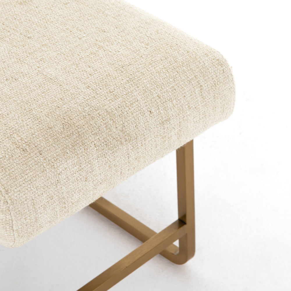 Beige upholstered stool with gold metal legs on a white background
