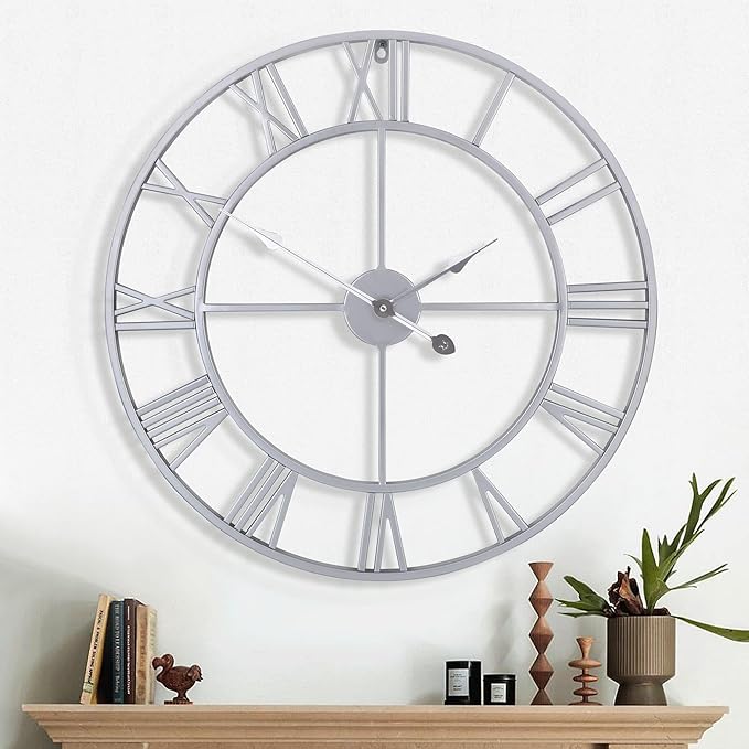 Large silver wall clock on a white wall with a decorative shelf below.