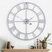 Large silver wall clock on a white wall with a decorative shelf below.