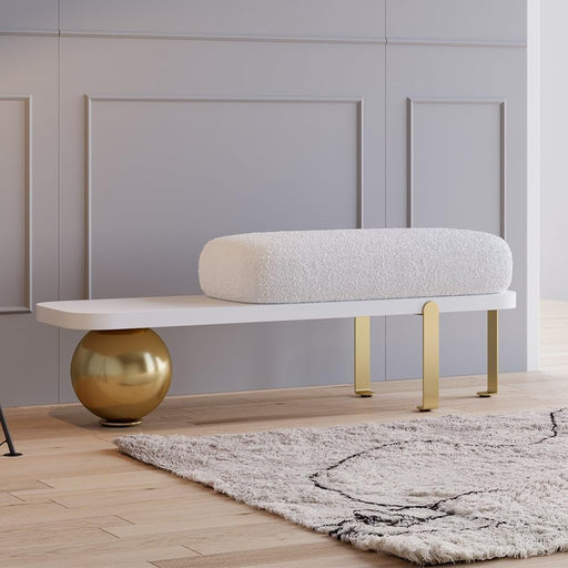 Modern bench with gold legs and a spherical gold object on a wooden floor.