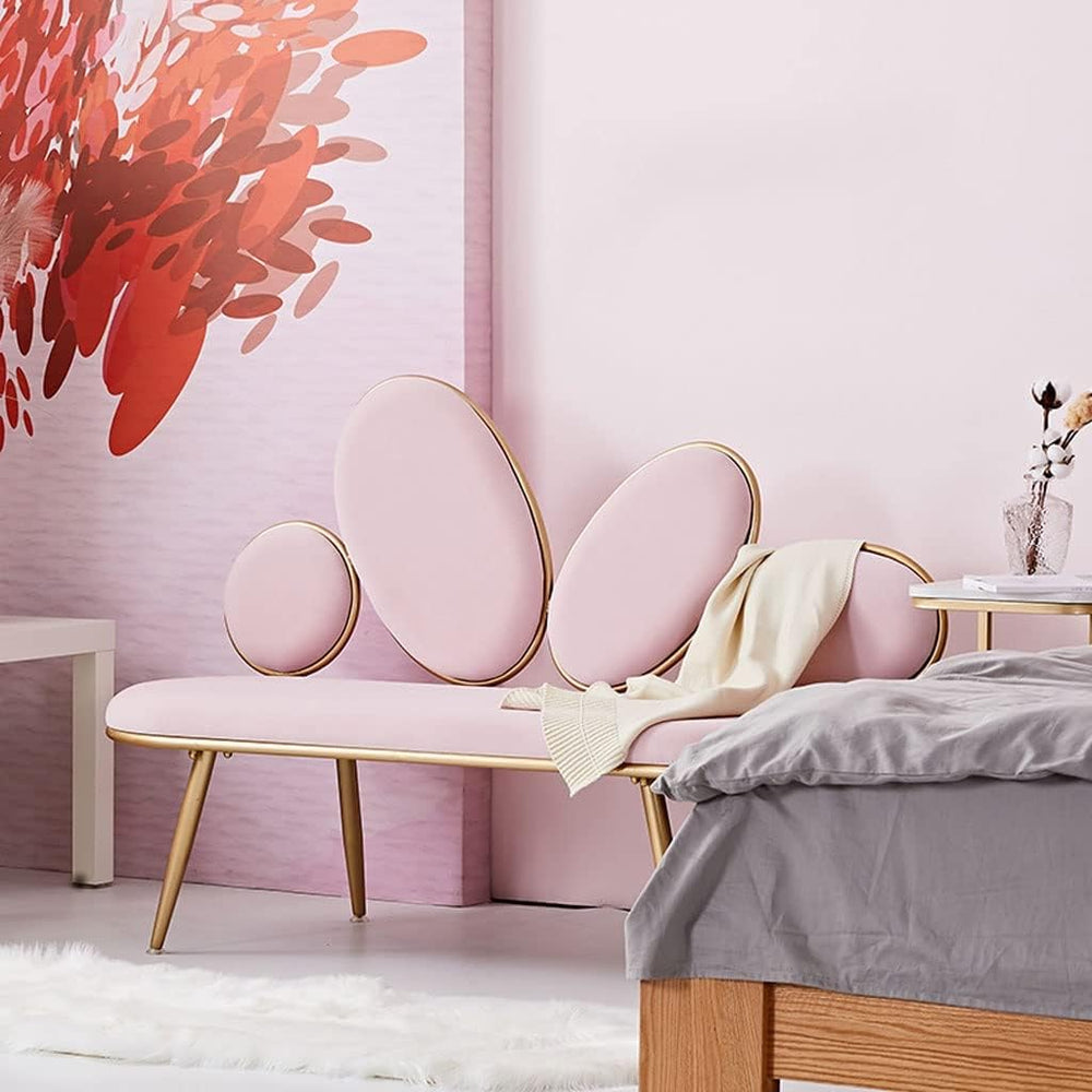 Pink upholstered bench with gold legs in a bedroom setting with a pink wall and bed.