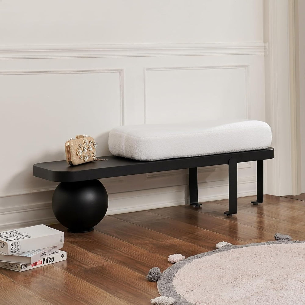 Black bench with a white cushion in a room with wooden floor and white walls.