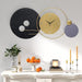 Decorative wall clock with modern design on a white wall above a table with candles and fruit.