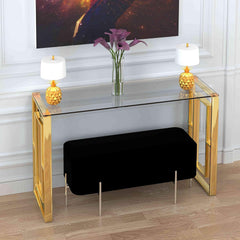 Glass console table with gold frame, black bench, and decorative items in a room setting.