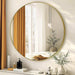 Round gold-framed mirror on a wall with decorative items below