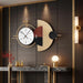 Decorative wall clock with abstract design on a dark wall with lighting fixtures.
