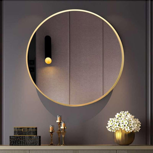 Round gold-framed mirror on a dark wall with decorative items below.