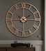 Large copper wall clock on a gray wall with a wooden cabinet below.