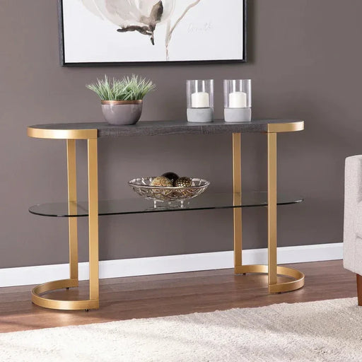 Console table with gold legs and glass shelves in a room setting.