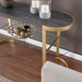 Console table with gold legs and dark surface, featuring decorative items on a wooden floor.
