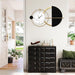 Modern wall clock with black and gold design on a white wall above a black cabinet.