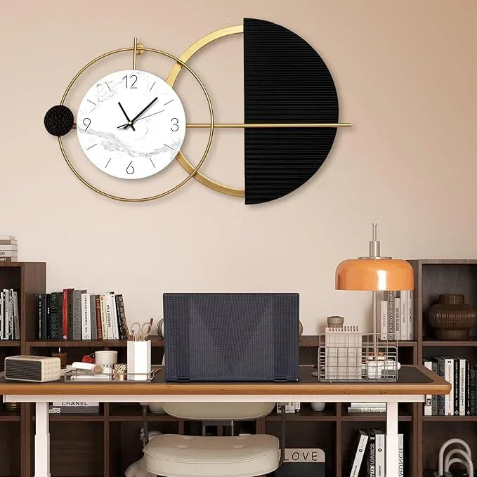 Modern wall clock with black and gold design on a beige wall above a desk.