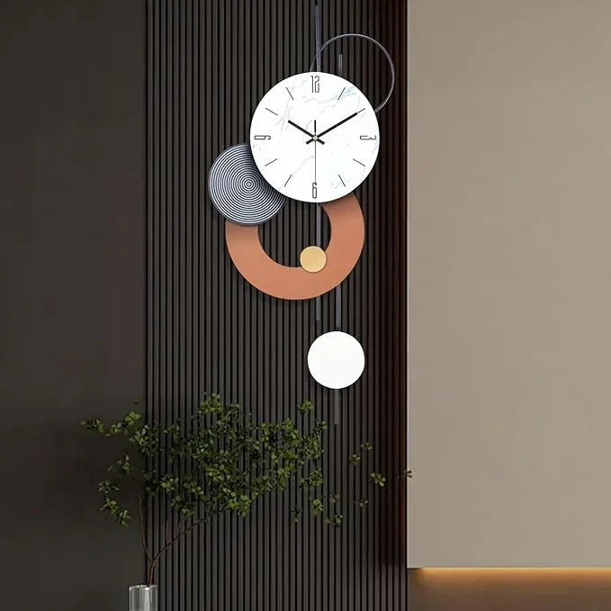 Modern wall clock with decorative elements on a wall with a plant in the foreground.