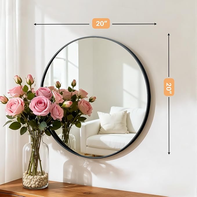 Round mirror with black frame on a wall, next to a vase of pink roses.