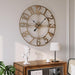 Large antique wall clock on a wall above a wooden console table with a lamp and statue.