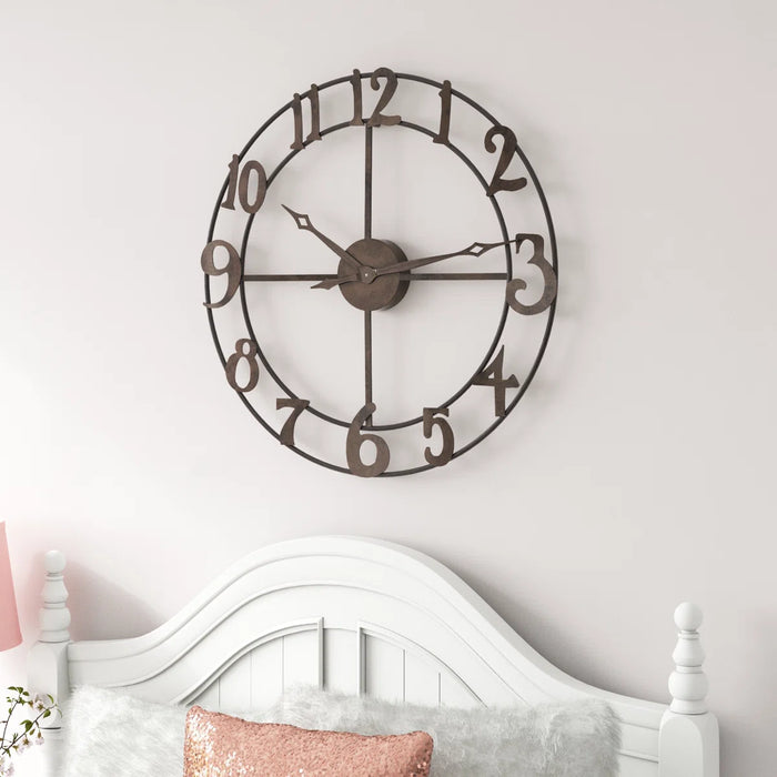 Large decorative wall clock on a white wall above a bed with pink and gray pillows.