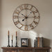 antique wall clock with candles and books on a wooden surface against a beige wall.