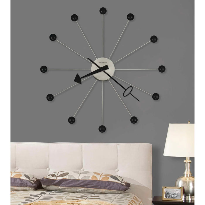 Modern wall clock with black and silver design on a gray wall above a sofa.