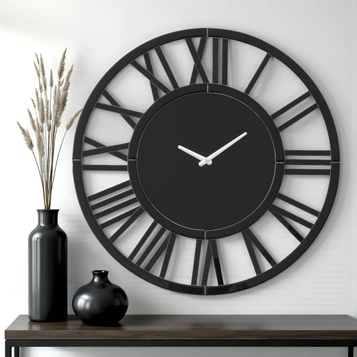Large black wall clock with Roman numeral design on a white wall, accompanied by two black vases.