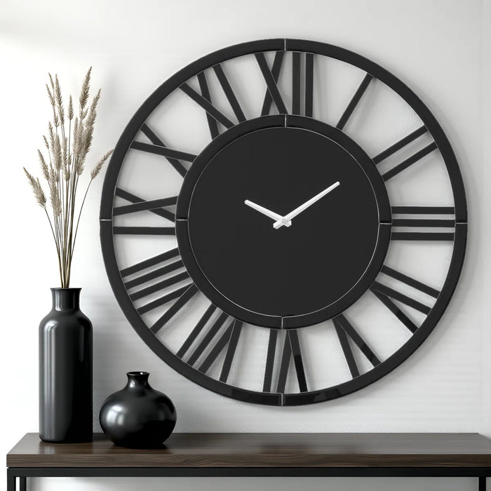 Large black wall clock with Roman numeral design on a white wall, accompanied by two black vases.