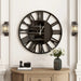 Large black wall clock with Roman numerals on a white wall above a wooden console table.
