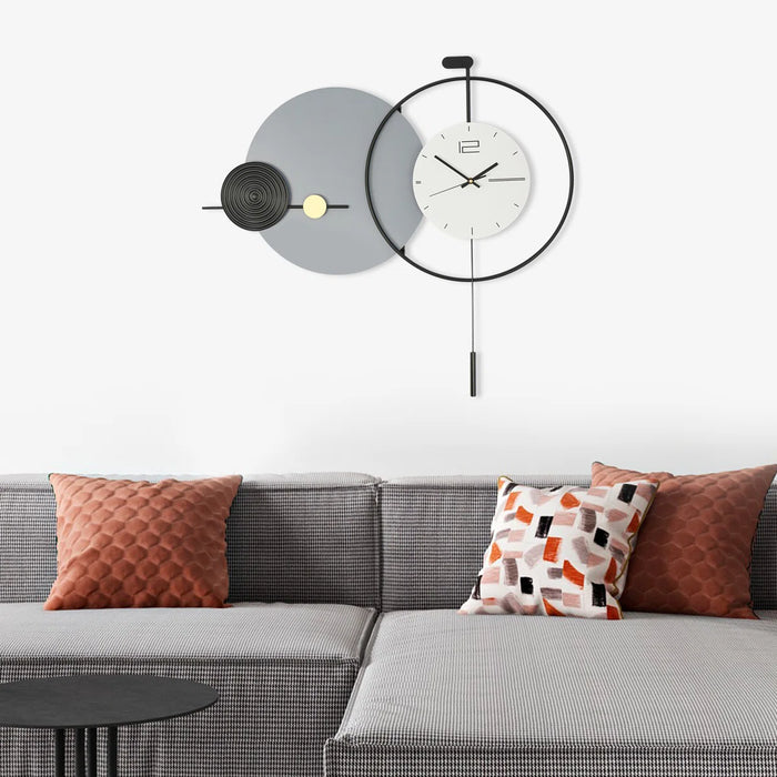 Modern wall clock with decorative design above a gray sofa with colorful cushions.