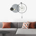 Modern wall clock with decorative design above a gray sofa with colorful cushions.