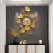 Decorative gold leaf wall clock on a dark gray wall with a console table and decorative items.