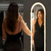 Woman trying on a black dress in front of a floor led mirror.