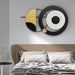 Decorative wall clock with gold and black design above a bed in a bedroom setting.