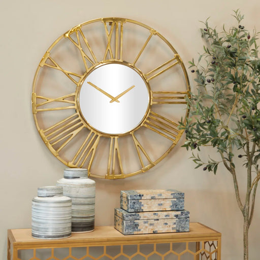 Gold wall clock with Roman numeral design on a wall with decorative items below.
