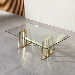 Glass coffee table with gold metal legs on a concrete floor.