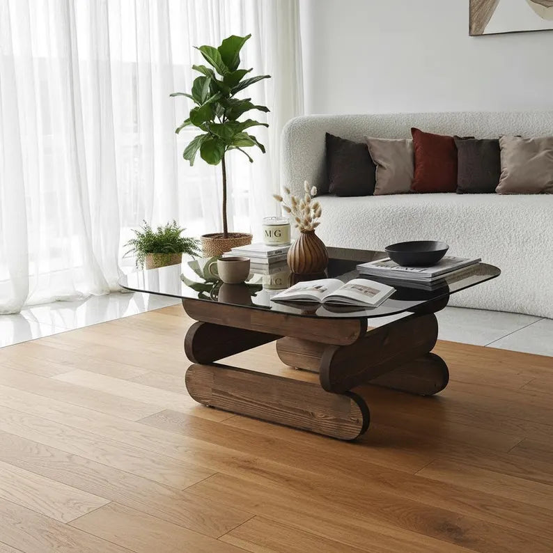 Modern living room with a glass coffee table, books, and a plant.