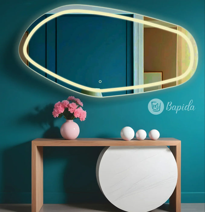 irregular mirror with LED lighting on a teal wall above a wooden console table.