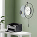 Modern wall clock on a green wall with a printer on a table below.