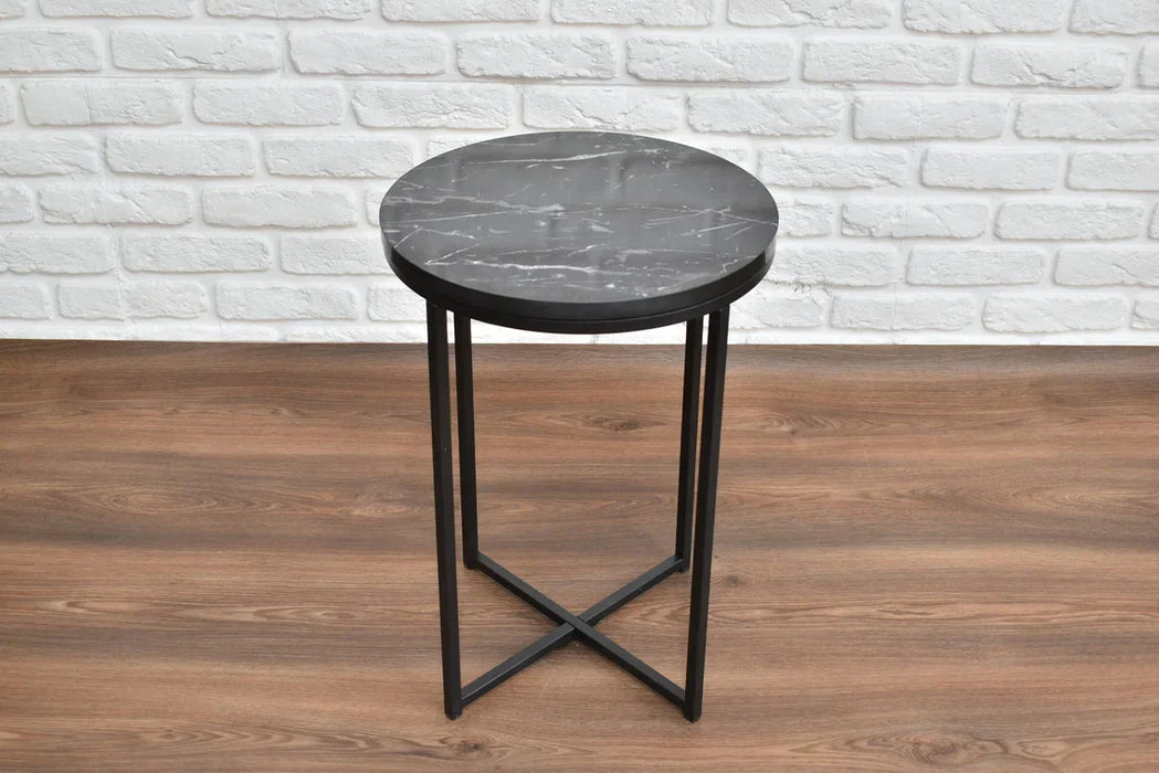 Round side table with marble top and black metal legs against a white brick wall.