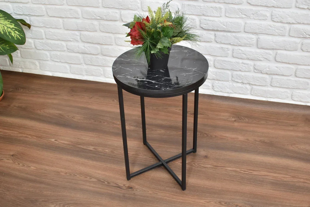 Round black marble bedside table with metal legs against a white brick wall.