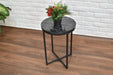 Round black marble bedside table with metal legs against a white brick wall.