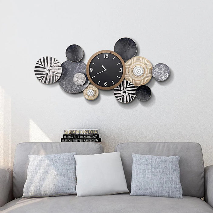 Decorative wall clock with circular designs on a white wall above a gray sofa.