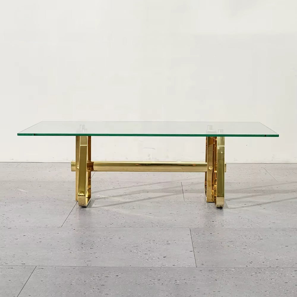 Glass coffee table with gold metal legs on a light wooden floor.