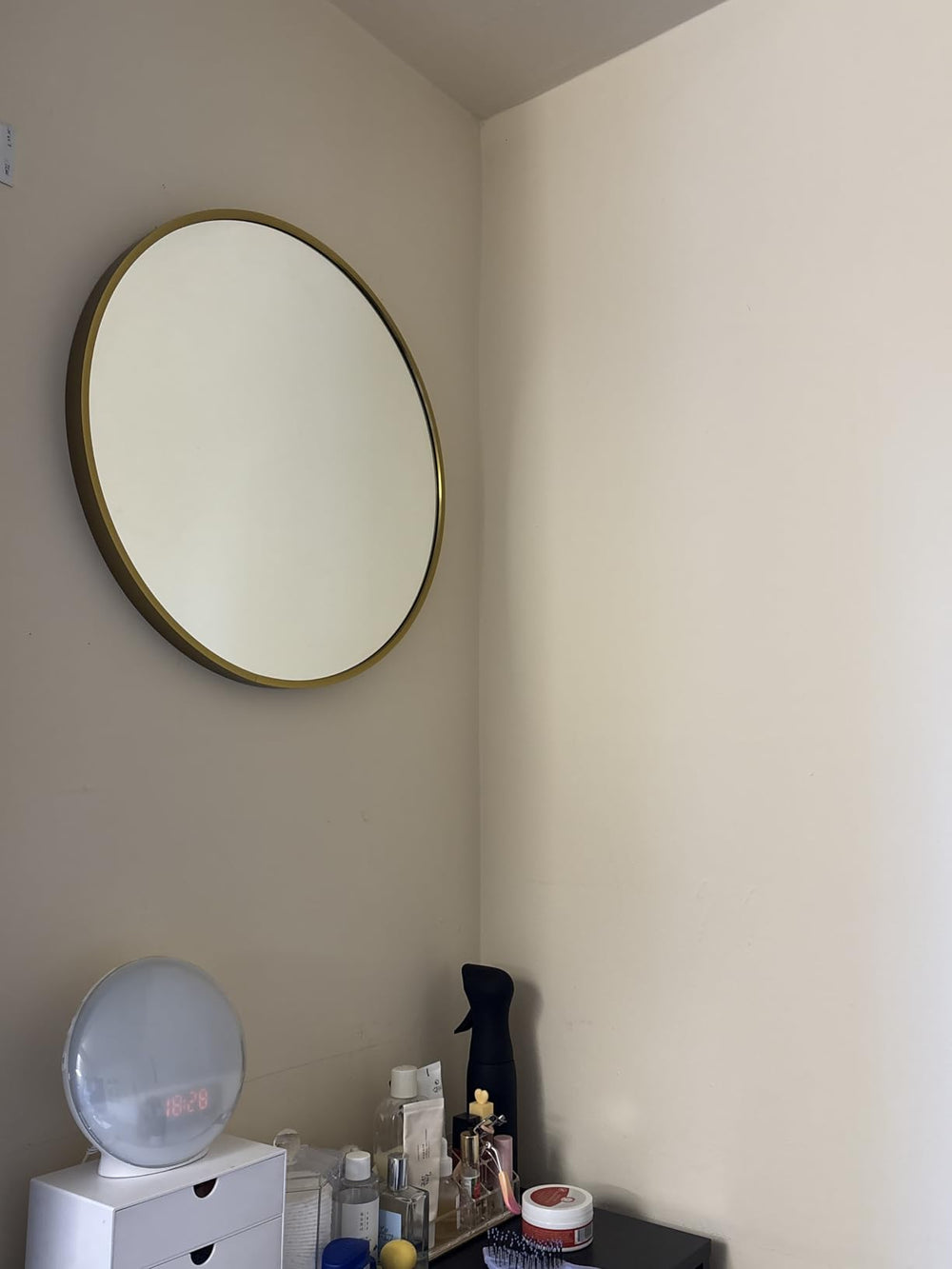 Round mirror with gold frame on a beige wall above a white dresser.