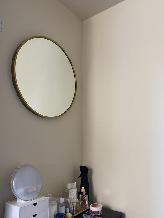 Round mirror with gold frame on a beige wall above a white dresser.