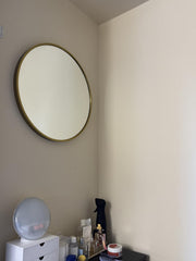 Round mirror with gold frame on a beige wall above a white dresser.